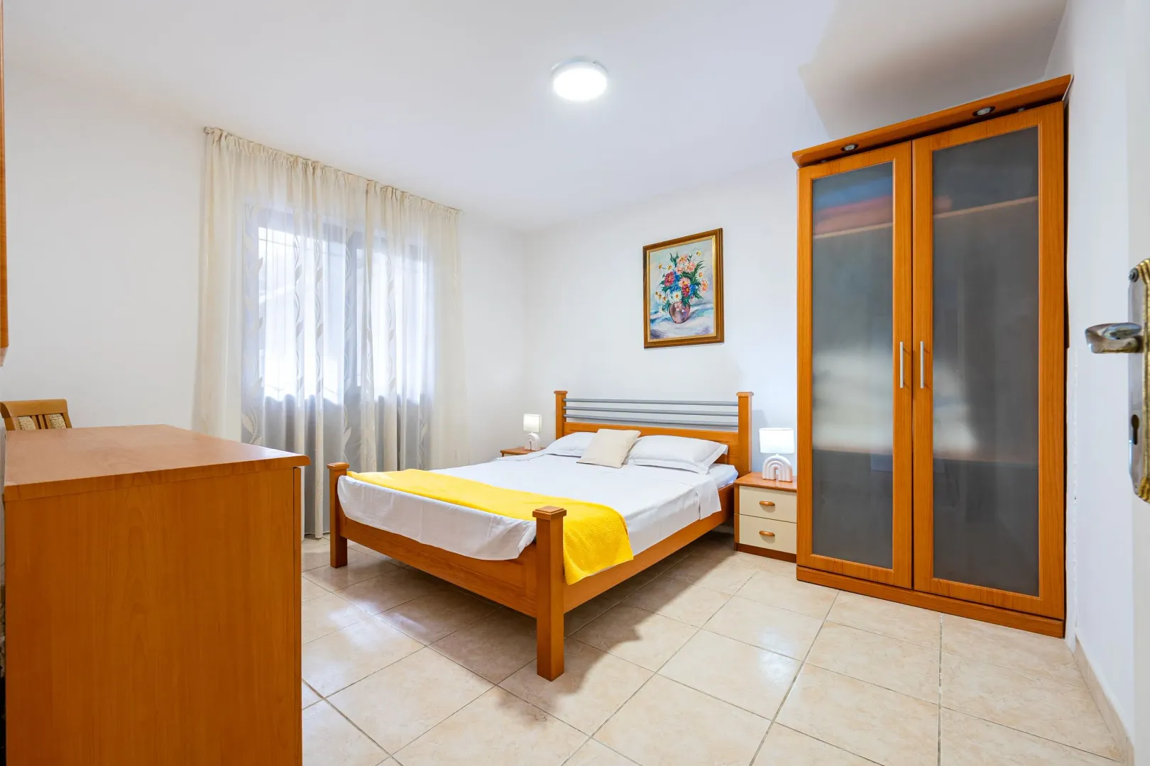 Furnished bedroom with a double bed, wooden wardrobe, and a window.