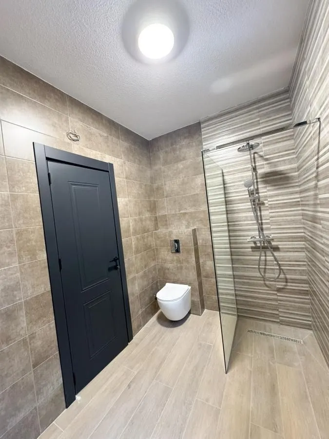 Kupatilo obloženo keramičkim pločicama sa tuš kabinom i wc šoljom.