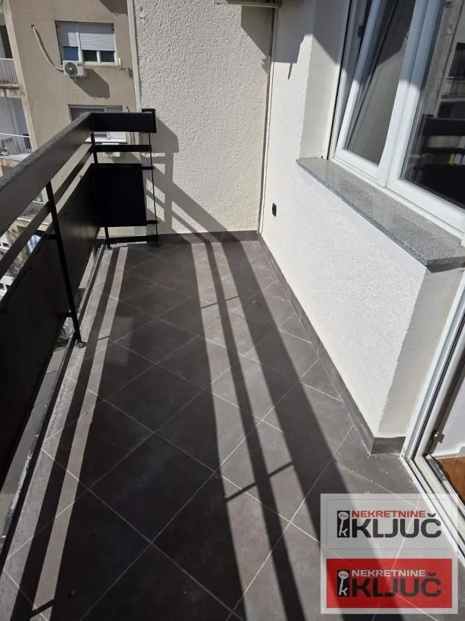 Pogled na prostrani balkon sa tamnim pločicama i metalnom ogradom.
