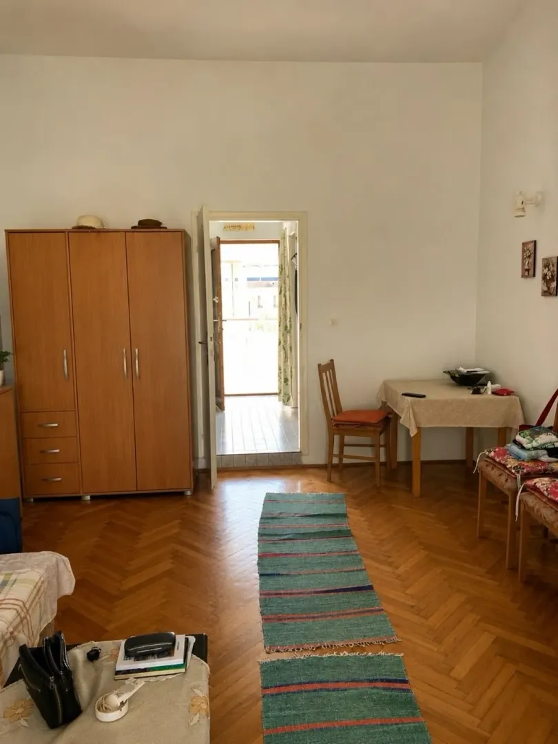 Dnevna soba sa drvenim ormarom, stolom i izlazom na terasu.