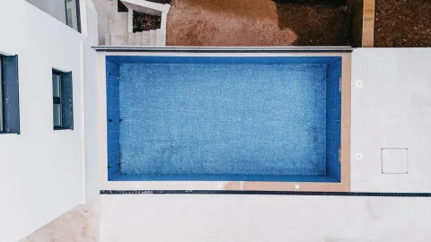 Pogled odozgo na spoljni bazen sa plavim pločicama i popločanim dvorištem. - image 6