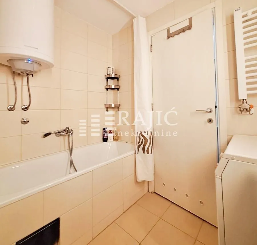 Small bathroom with a bathtub, water heater, and white ceramic tiles.