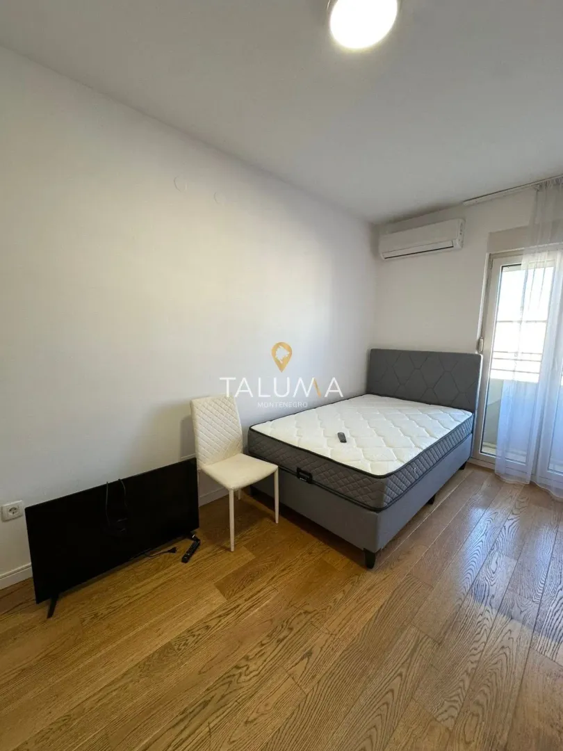 Spavaća soba sa bračnim krevetom, klima uređajem i izlazom na balkon.