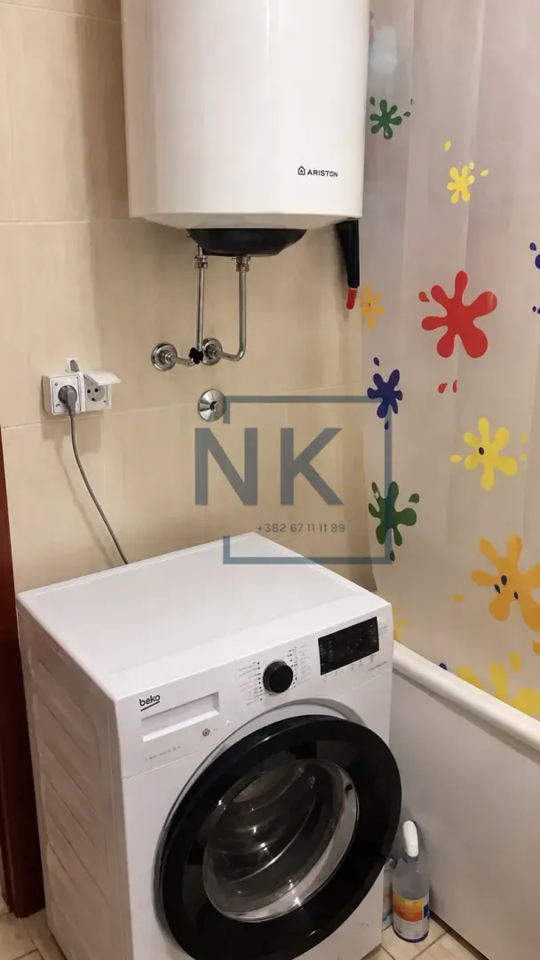 Kupatilo sa veš mašinom, bojlerom i kadom sa šarenom zavjesom.