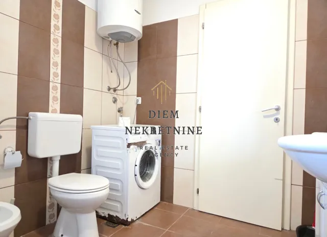 Small tiled bathroom with a toilet, washing machine, and water heater.