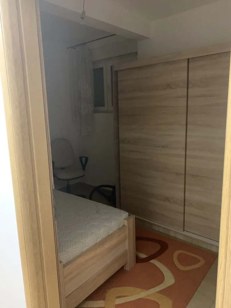 A small bedroom with a wooden bed and a large wardrobe viewed through a doorway.