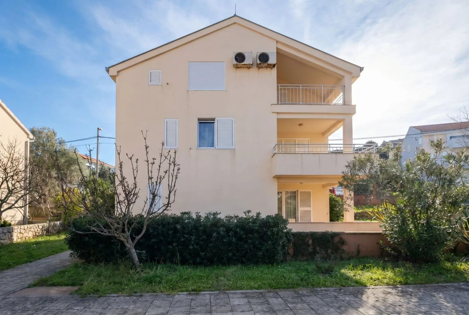 Vanjski izgled trospratne kuće sa balkonima i malim dvorištem.