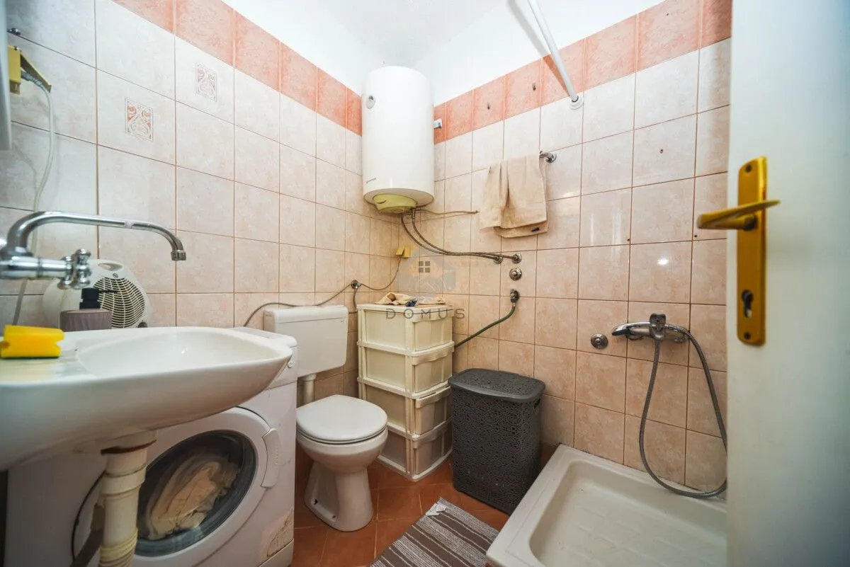 Smaller tiled bathroom equipped with a washbasin, washing machine, toilet, and shower tray.