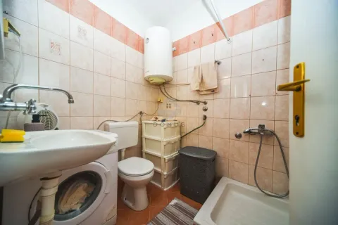 Smaller tiled bathroom equipped with a washbasin, washing machine, toilet, and shower tray. - image 8
