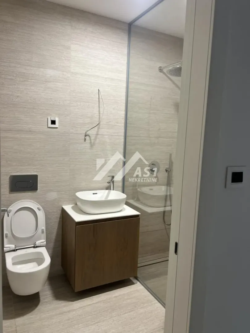 Modern bathroom with a walk-in shower, washbasin, and wall-mounted toilet.