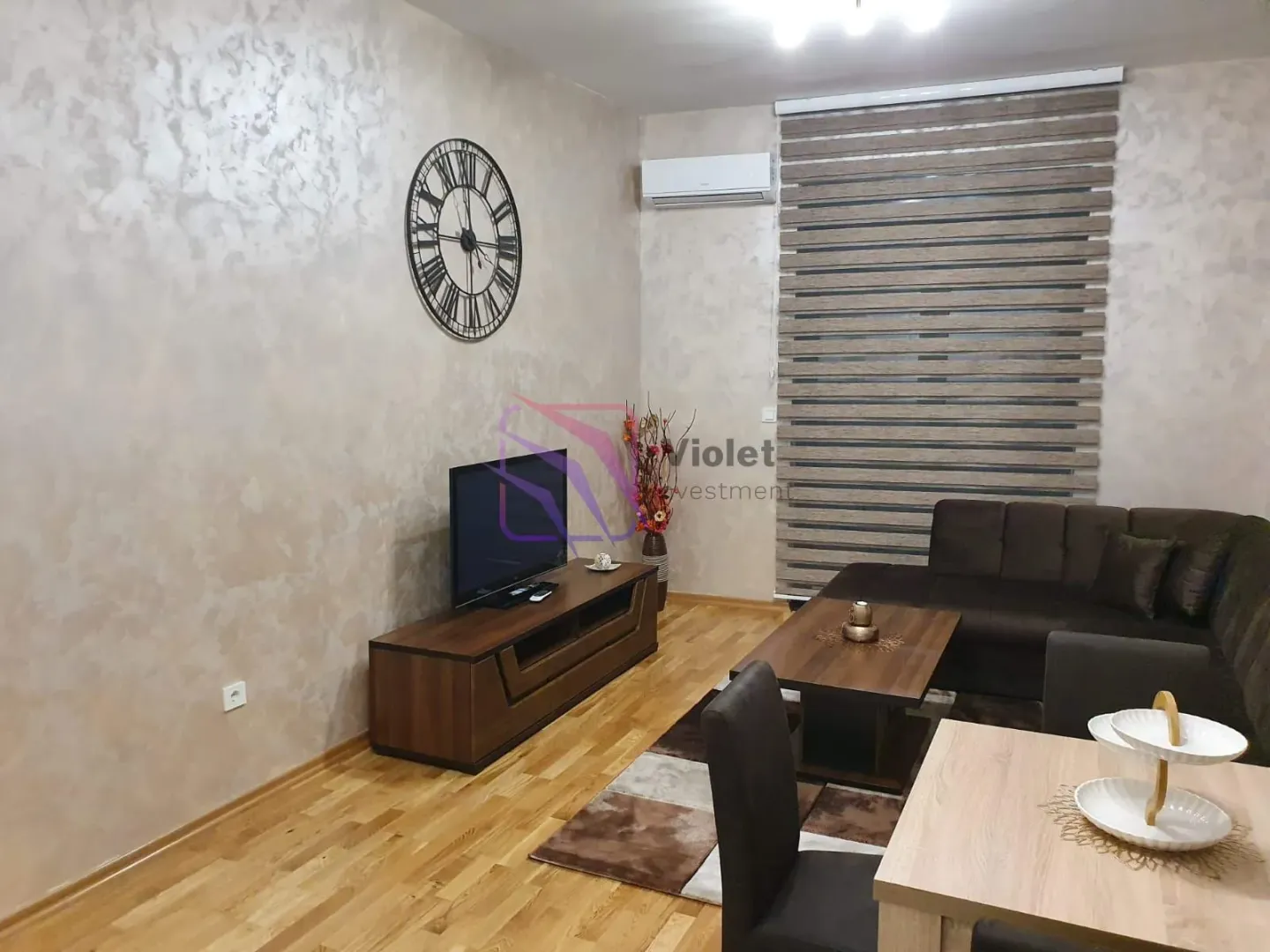 Living room furnished with a sofa, TV unit, and dining table.