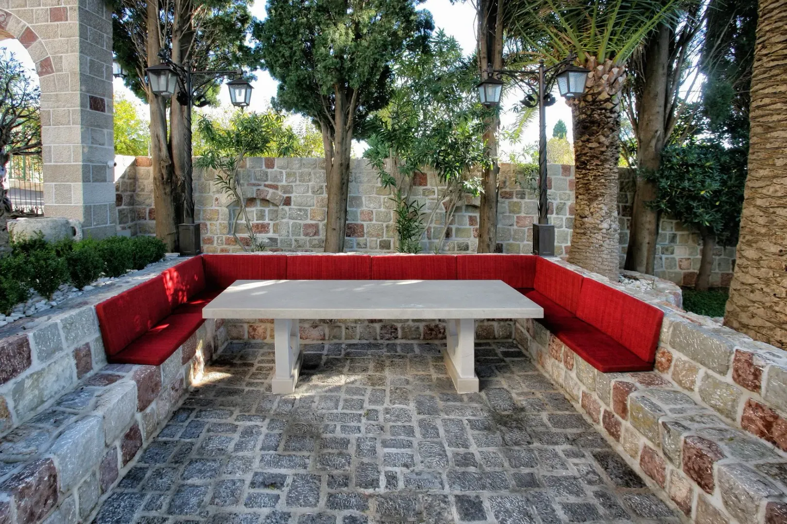 Outdoor seating area with a stone table, benches with red cushions, and a paved yard.