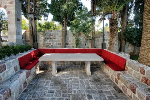 Outdoor seating area with a stone table, benches with red cushions, and a paved yard. - image 18