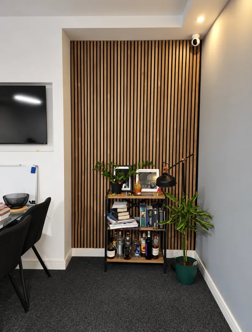 Corner of the room with wooden wall slats, a shelving unit, and plants.