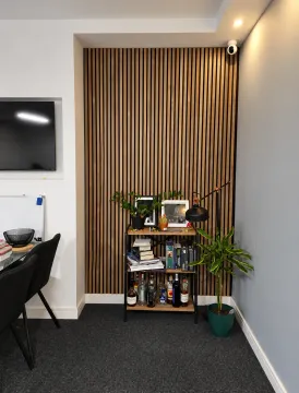 Corner of the room with wooden wall slats, a shelving unit, and plants. - image 8