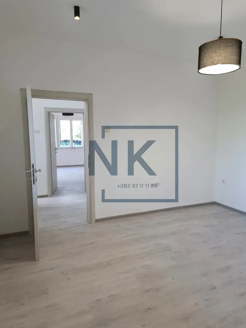 Empty room with light laminate flooring and an open door leading to another room.