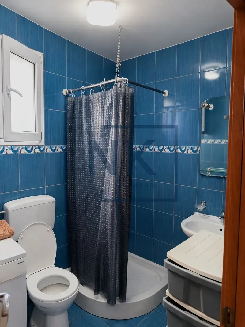 Kupatilo obloženo plavim pločicama sa tuš kabinom, WC šoljom i umivaonikom.