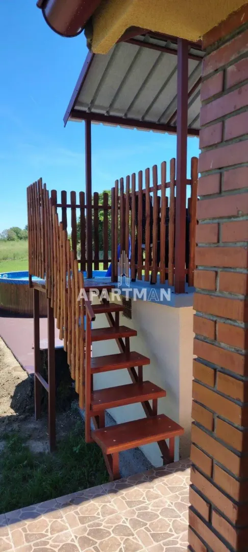 Drvene stepenice vode do natkrivene terase sa drvenom ogradom u dvorištu.