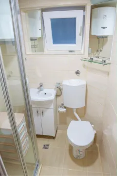 Small bathroom with light tiles, sink, toilet, and shower cabin. - image 3