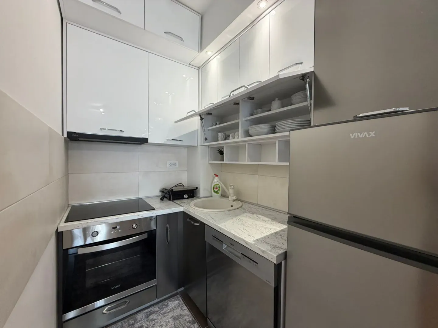 Small modern kitchen with white and grey cabinetry and built-in appliances.