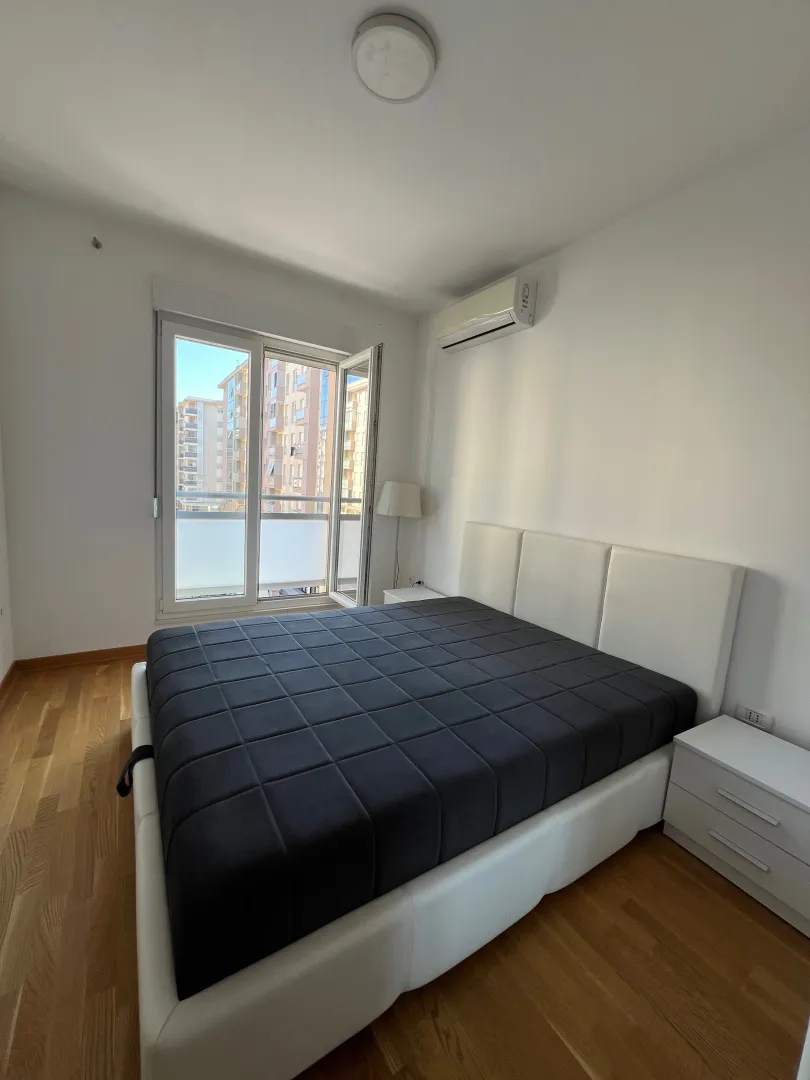 Bright bedroom with a double bed, white nightstands, and balcony doors.