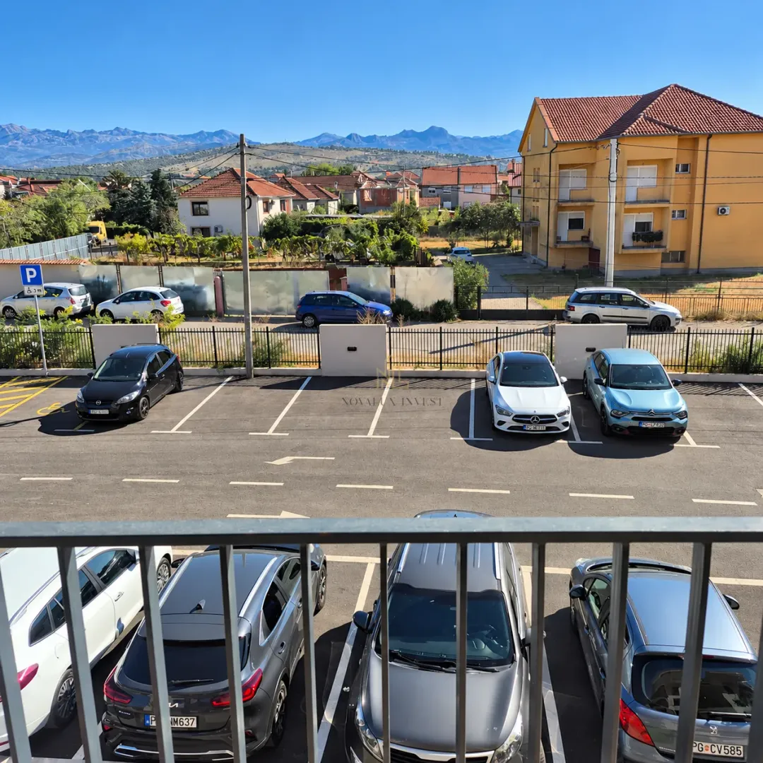 Pogled sa terase na parking i okolne zgrade sa planinama u pozadini.