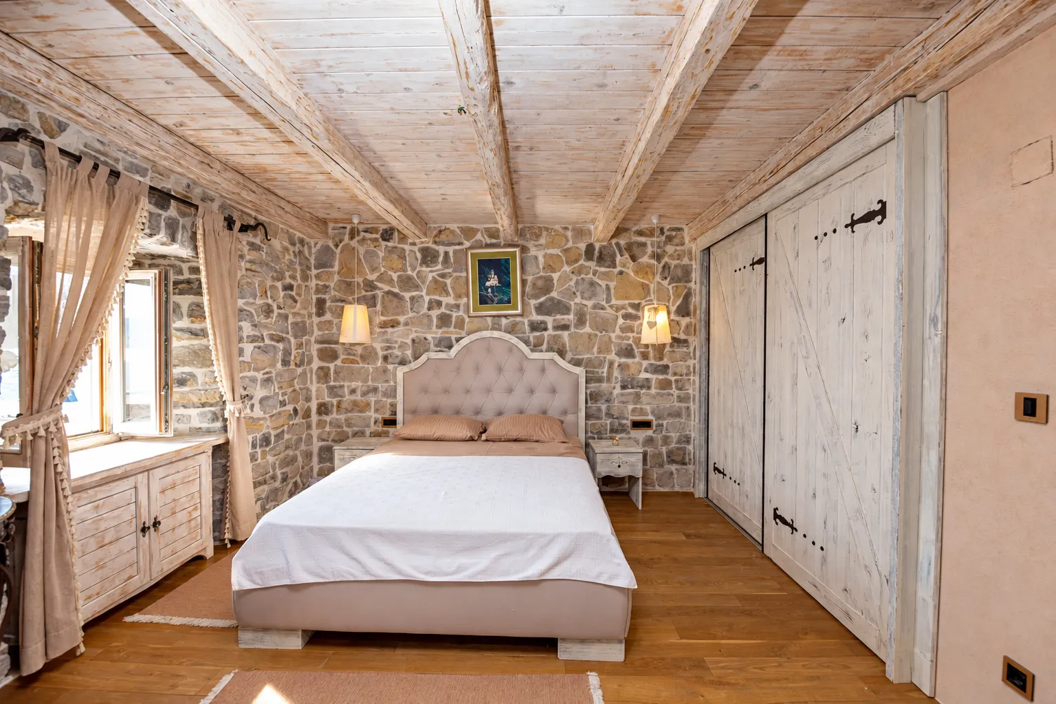 Rustic bedroom with a stone wall, wooden ceiling, and a double bed.