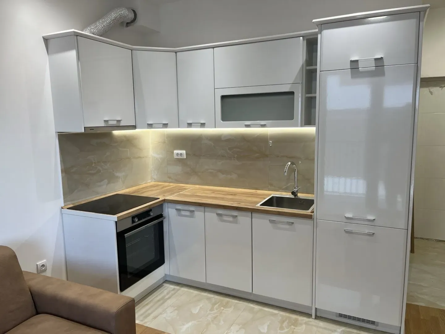 Moderna bijela kuhinja sa drvenom radnom površinom i ugradnim aparatima.