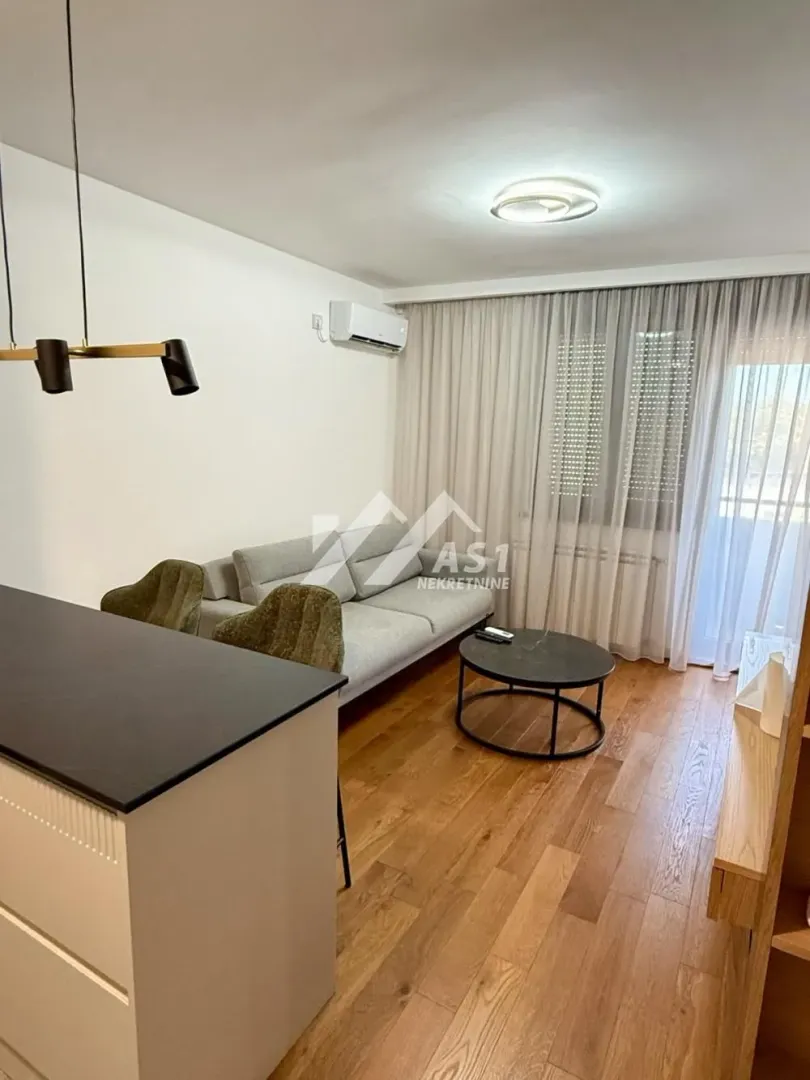 Dnevni boravak sa garniturom, stočićem i kuhinjskim elementima u prednjem planu.