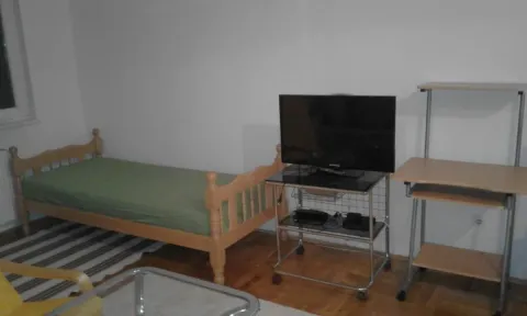 Manja spavaća soba sa krevetom, televizorom i radnim stolom. - image 3