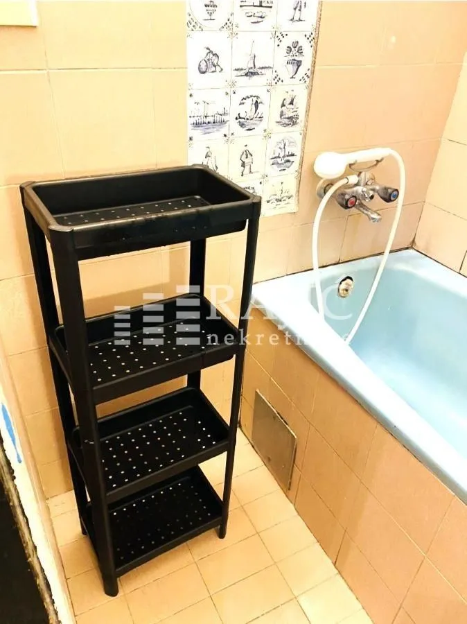 Small bathroom with a bathtub and a black plastic shelving unit.