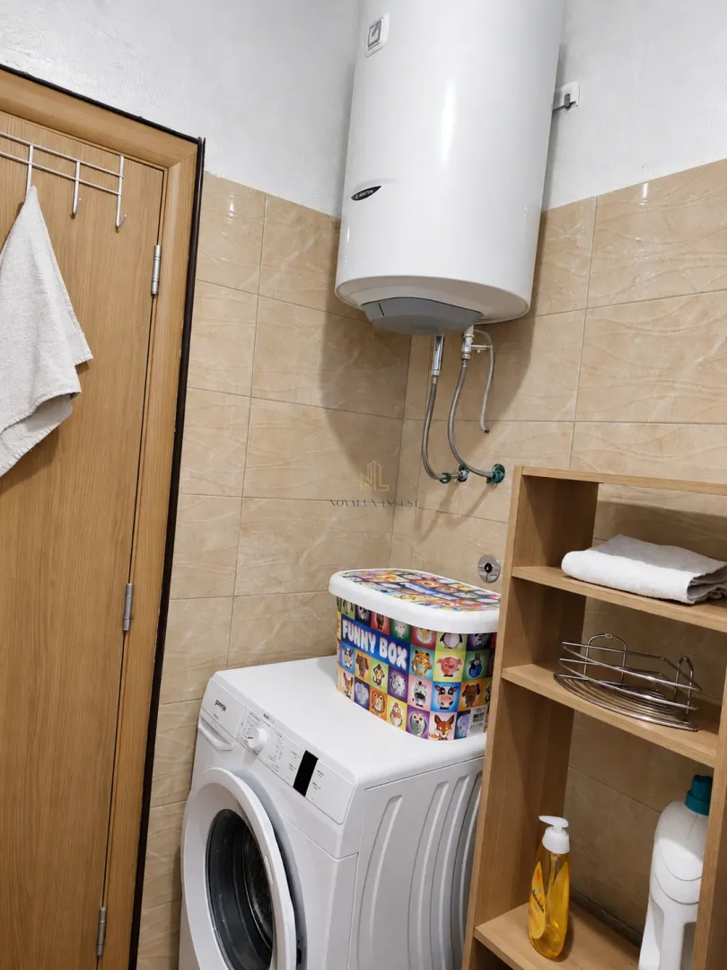 Bathroom with a washing machine, water heater, and a wooden shelf.