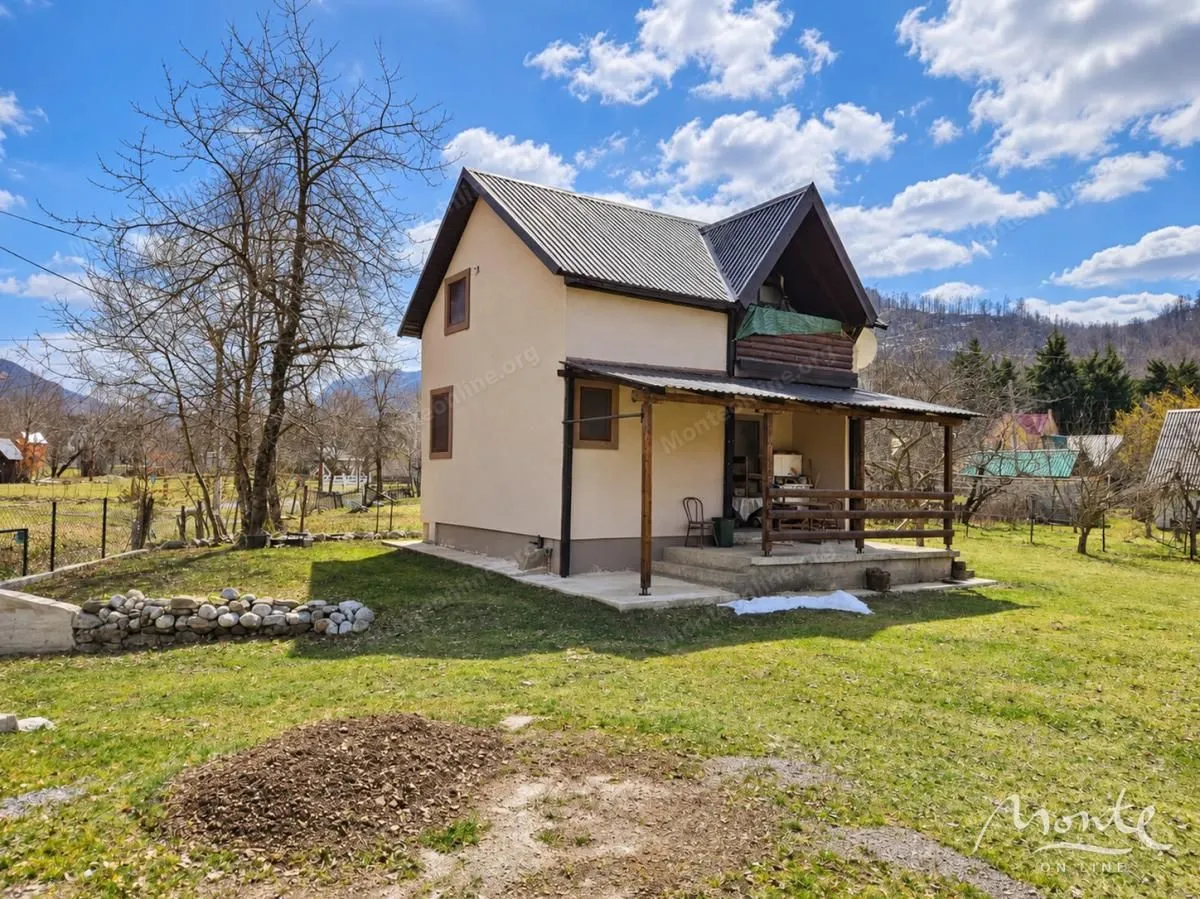 Pogled na dvorište i fasadu kuće sa trijemom u prirodnom okruženju.