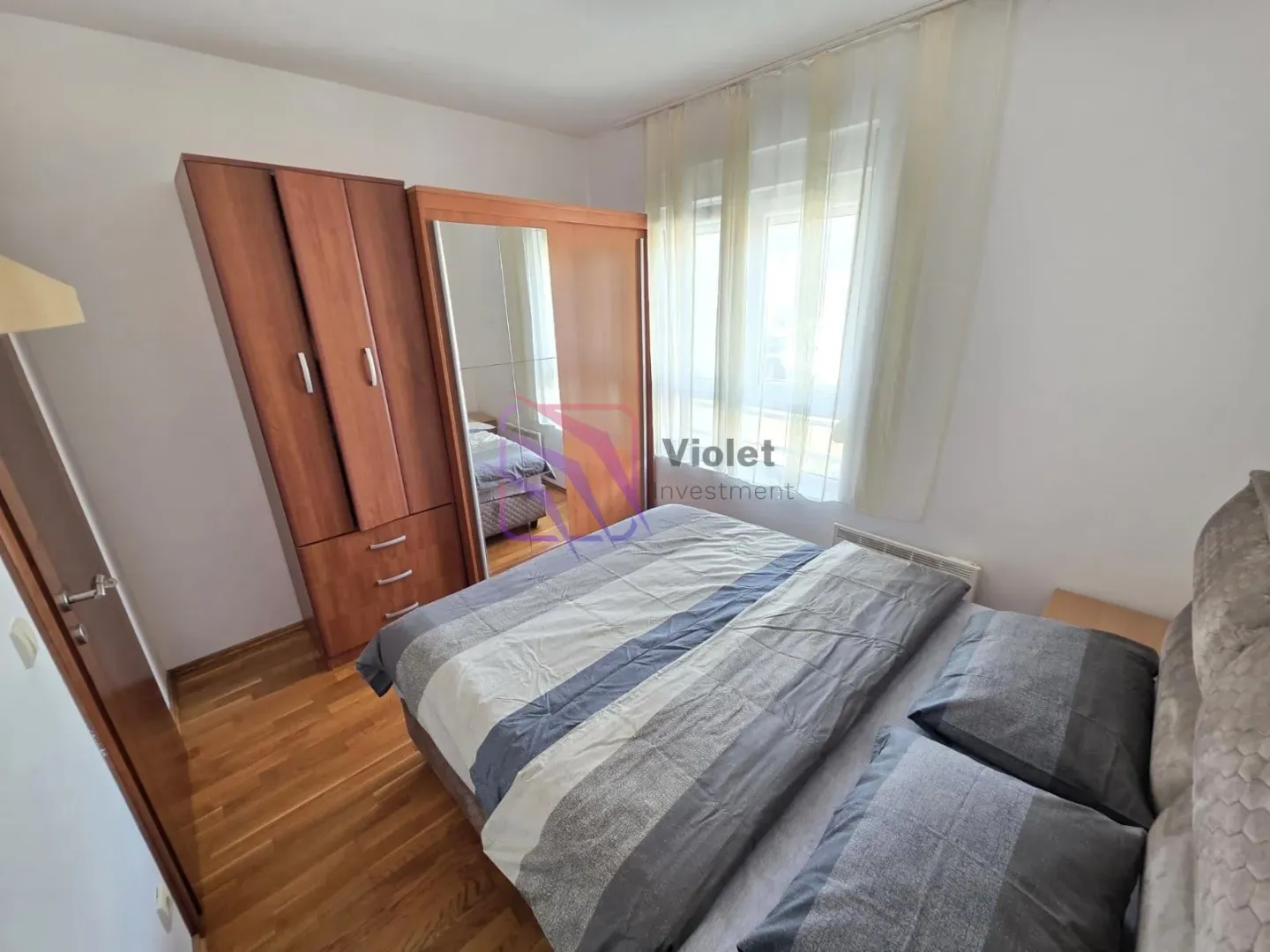 Furnished bedroom with a double bed, wooden wardrobe, and a window.