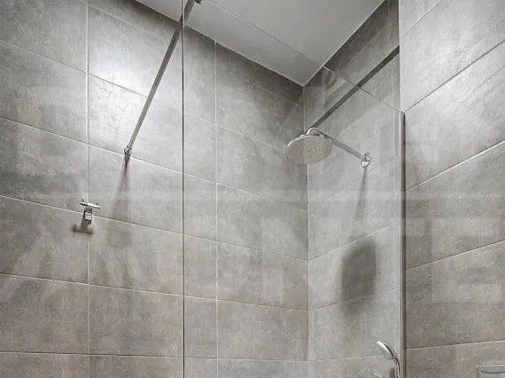 Walk-in shower with a glass partition in a bathroom finished with grey tiles.