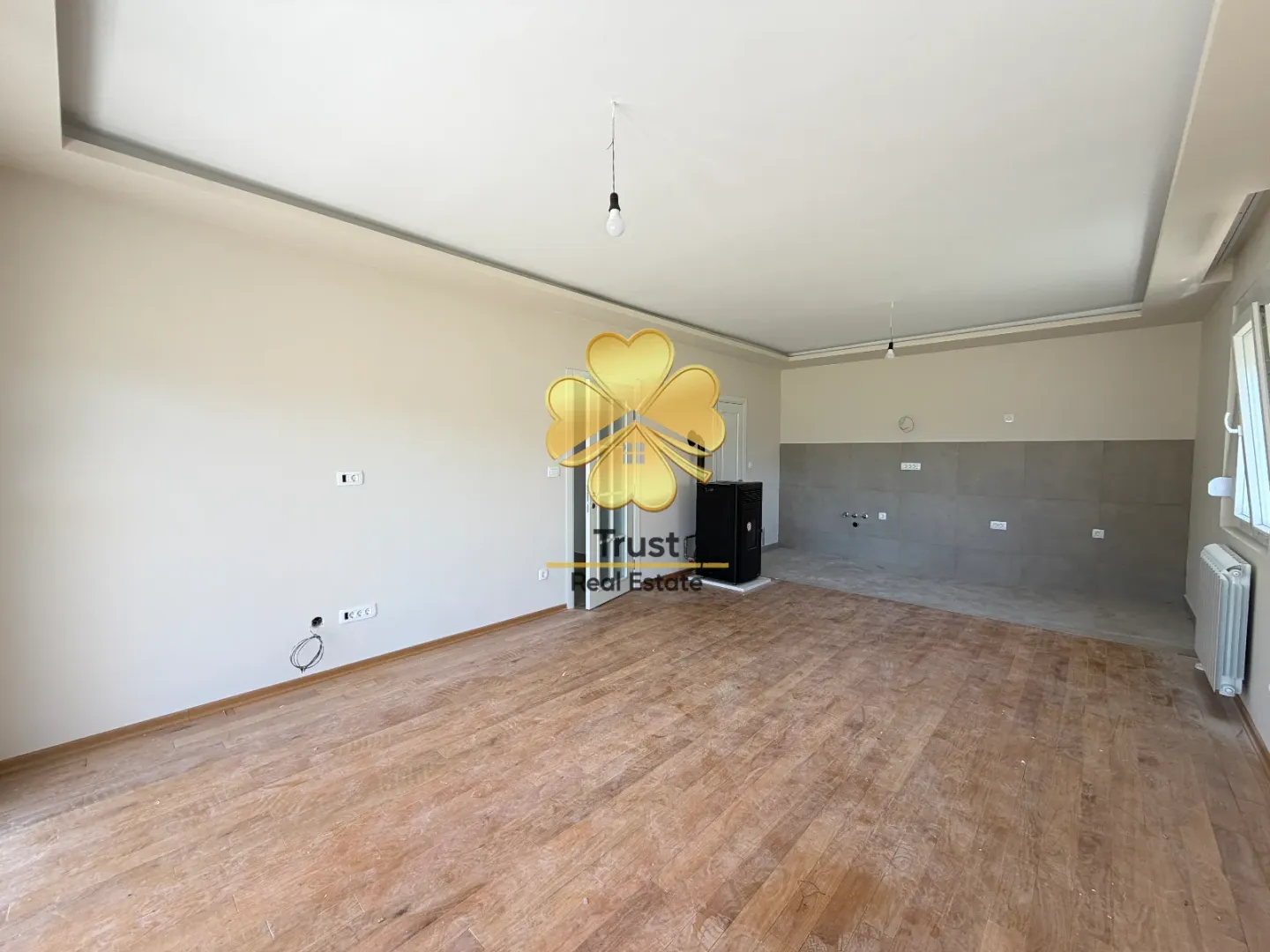 An empty room with hardwood flooring and tiles in the kitchen area.