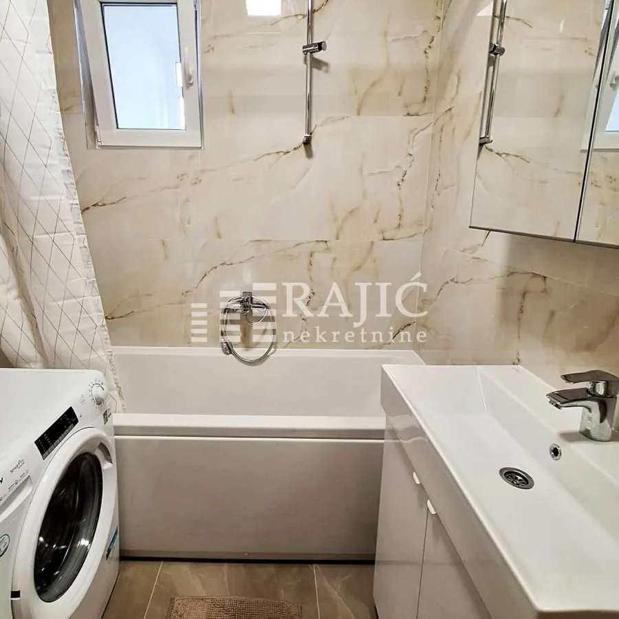 Modern bathroom with a bathtub, sink, and washing machine.