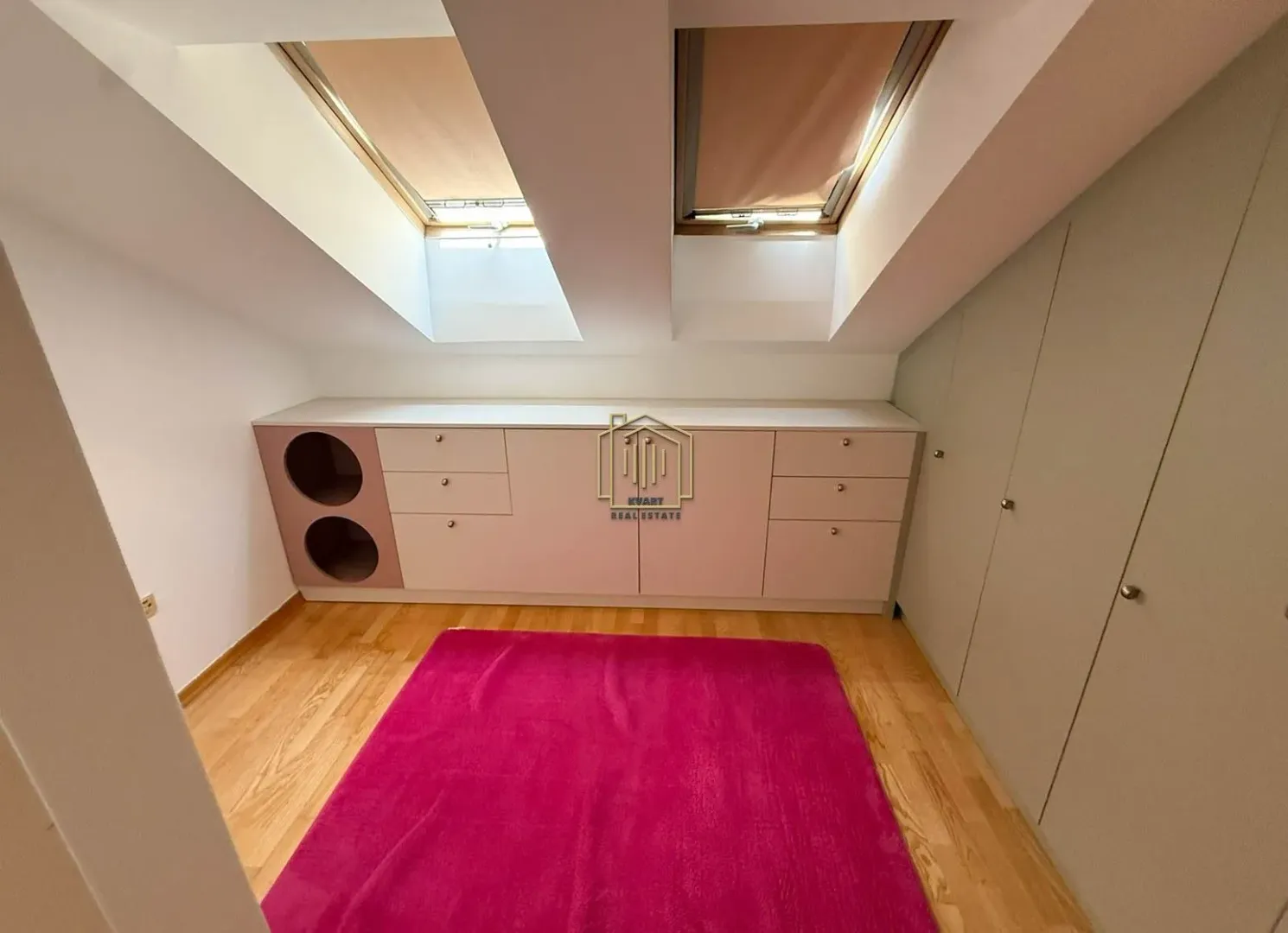 Attic room with skylights, built-in wardrobes, a chest of drawers, and a pink rug.