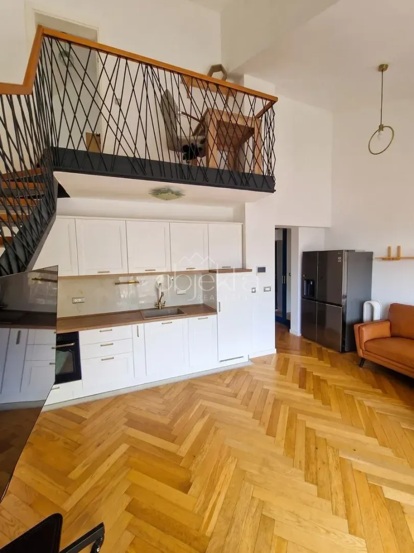 Dnevna soba sa kuhinjom, drvenim stepeništem i galerijom na spratu.