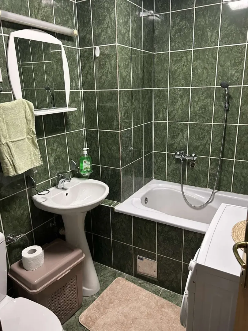 Kupatilo sa zelenim pločicama, kadom i umivaonikom.