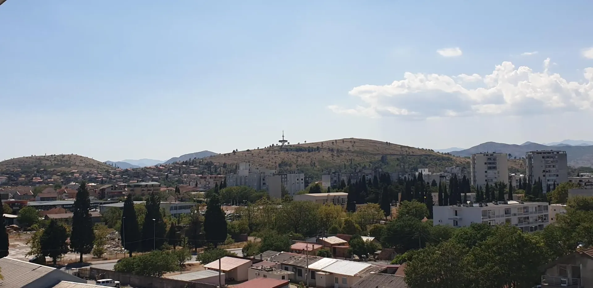 Panoramski pogled sa prozora na grad i brda u daljini.