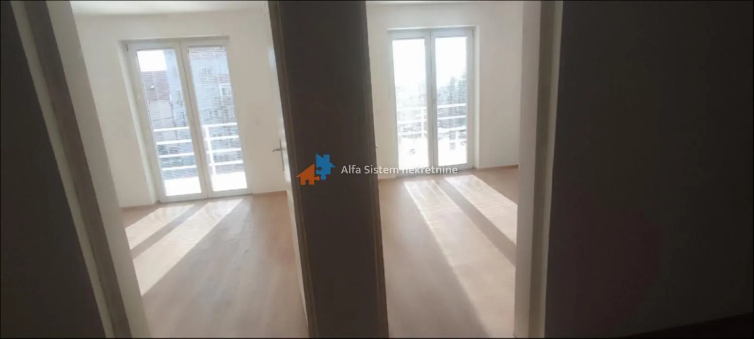 View from the hallway into two empty rooms with wooden flooring and balcony doors.