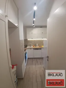 Pogled na manju kuhinju sa belim elementima i drvenom radnom pločom. - image 5