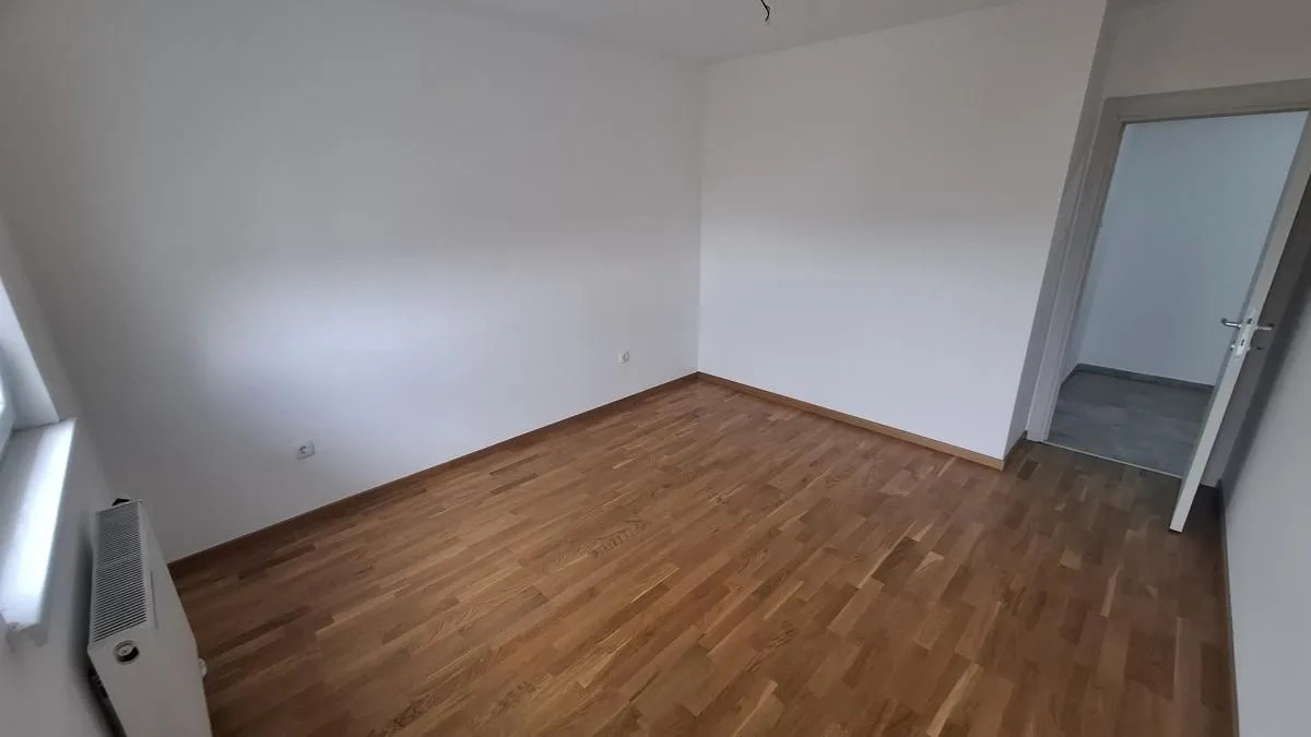 Prazna neopremljena prostorija sa drvenim podom i belim zidovima.