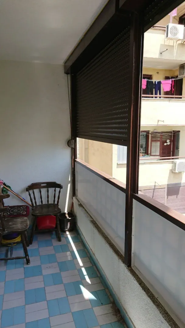 Zastakljena terasa sa drvenim stolicama i pločicama na podu.