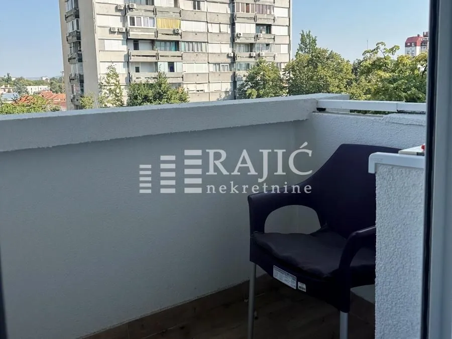 Small balcony with a chair and a view of surrounding buildings.
