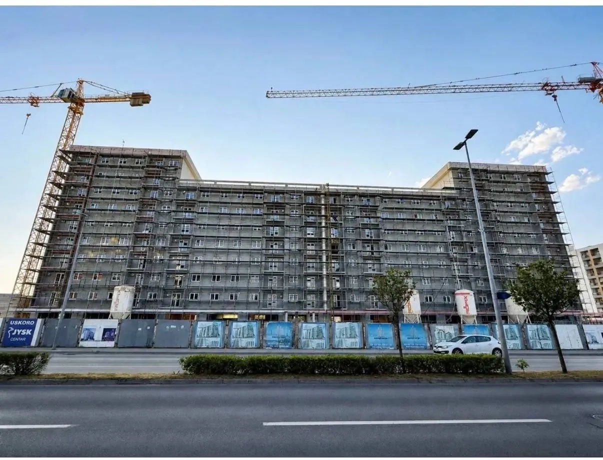 View of a residential building under construction with scaffolding and cranes.
