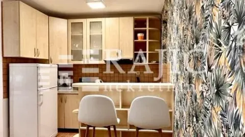 Small kitchen with light wood cabinets and a breakfast bar with two white chairs. - image 4