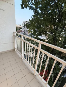 Pogled sa popločanog balkona sa belom ogradom na zelenilo i okolne zgrade. - image 20