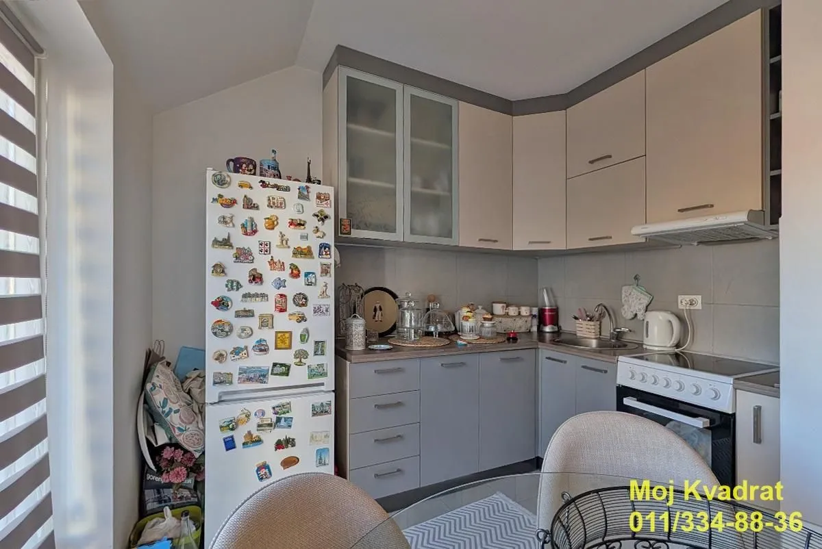 Small kitchen with grey and beige cabinets and a refrigerator covered in magnets.